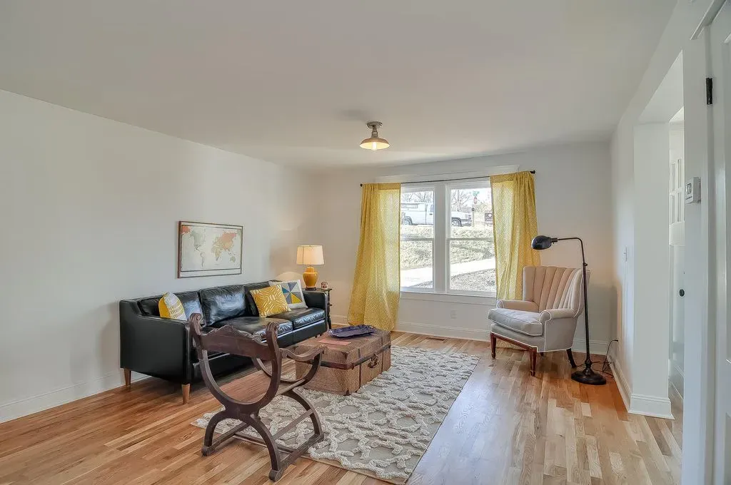 Bright living room with dark sofa, patterned rug, wicker chair, and large window with yellow curtains.