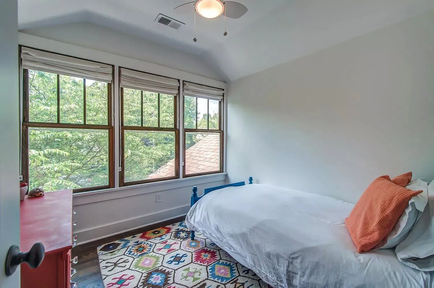 Bedroom with large windows, white bed, orange pillows, and colorful patterned rug