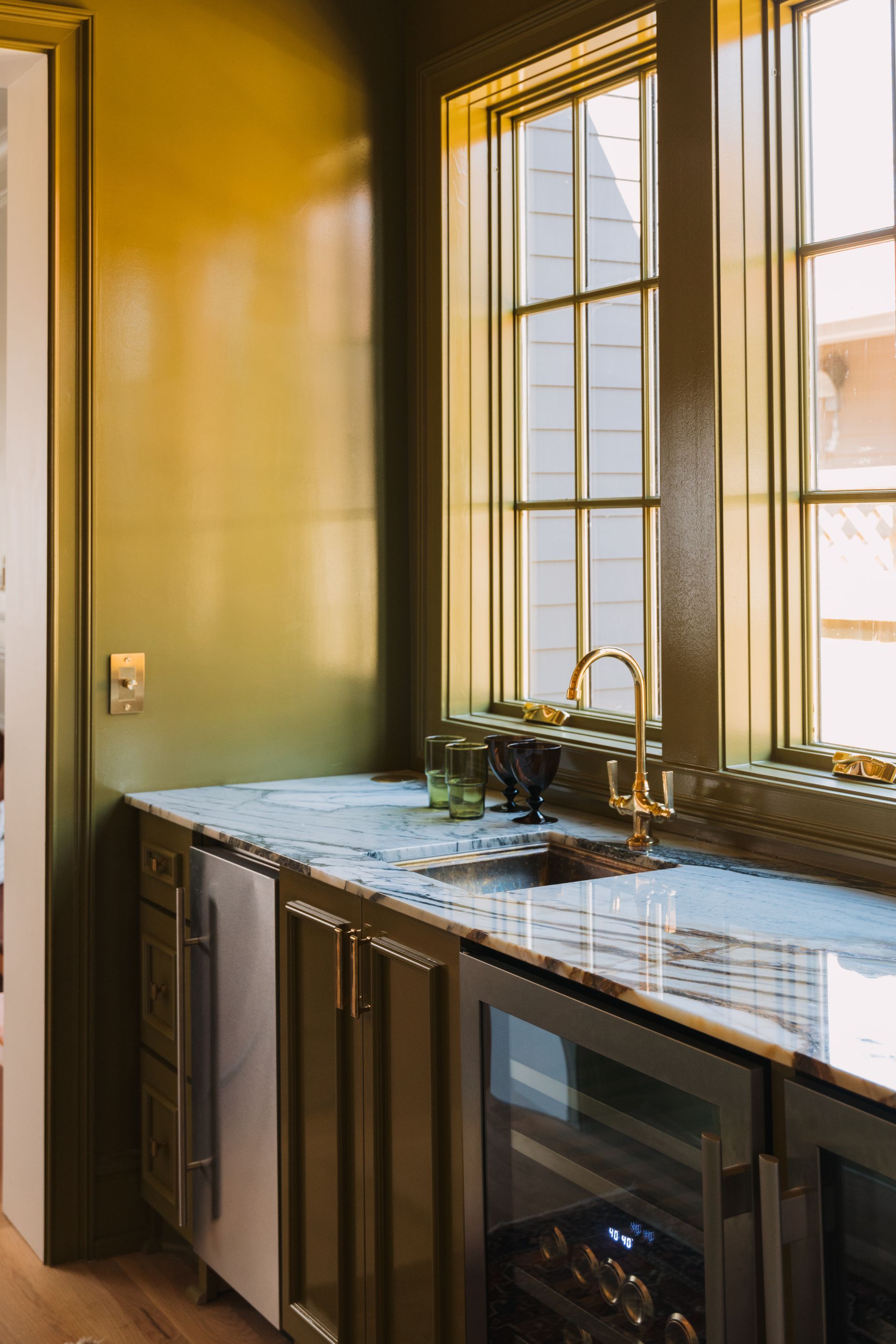 Modern kitchen sink under a tall window, with green walls and a blue-tiled countertop