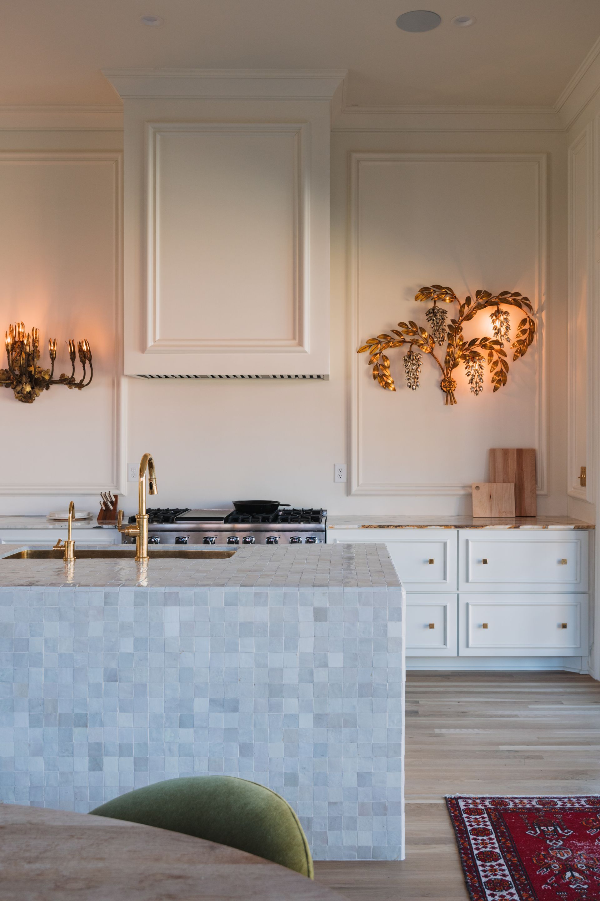 Elegant kitchen with white paneled walls, marble island, brass fixtures, and warm wall sconces