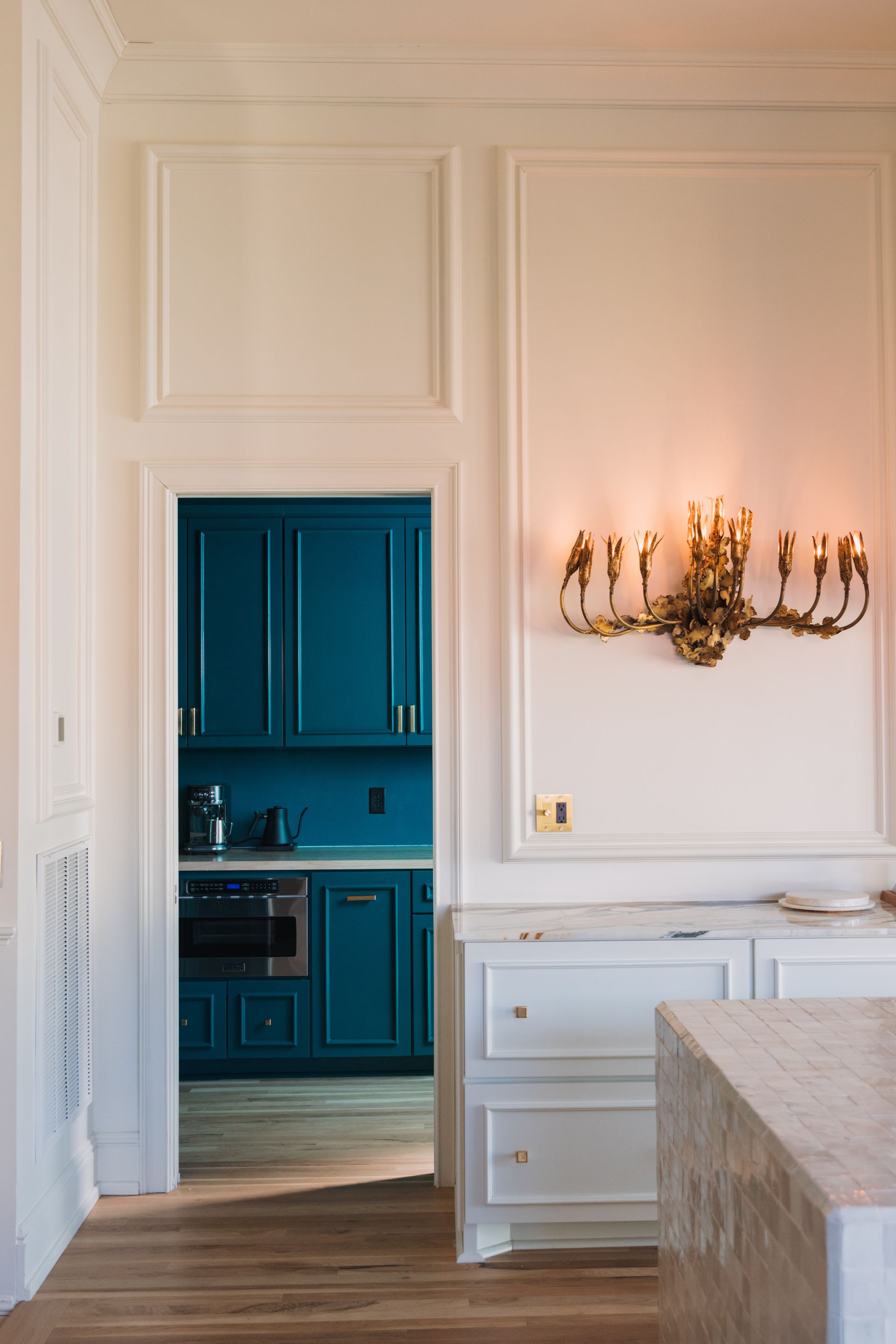 Elegant white dining room with wall sconces and blue kitchen visible through an open doorway