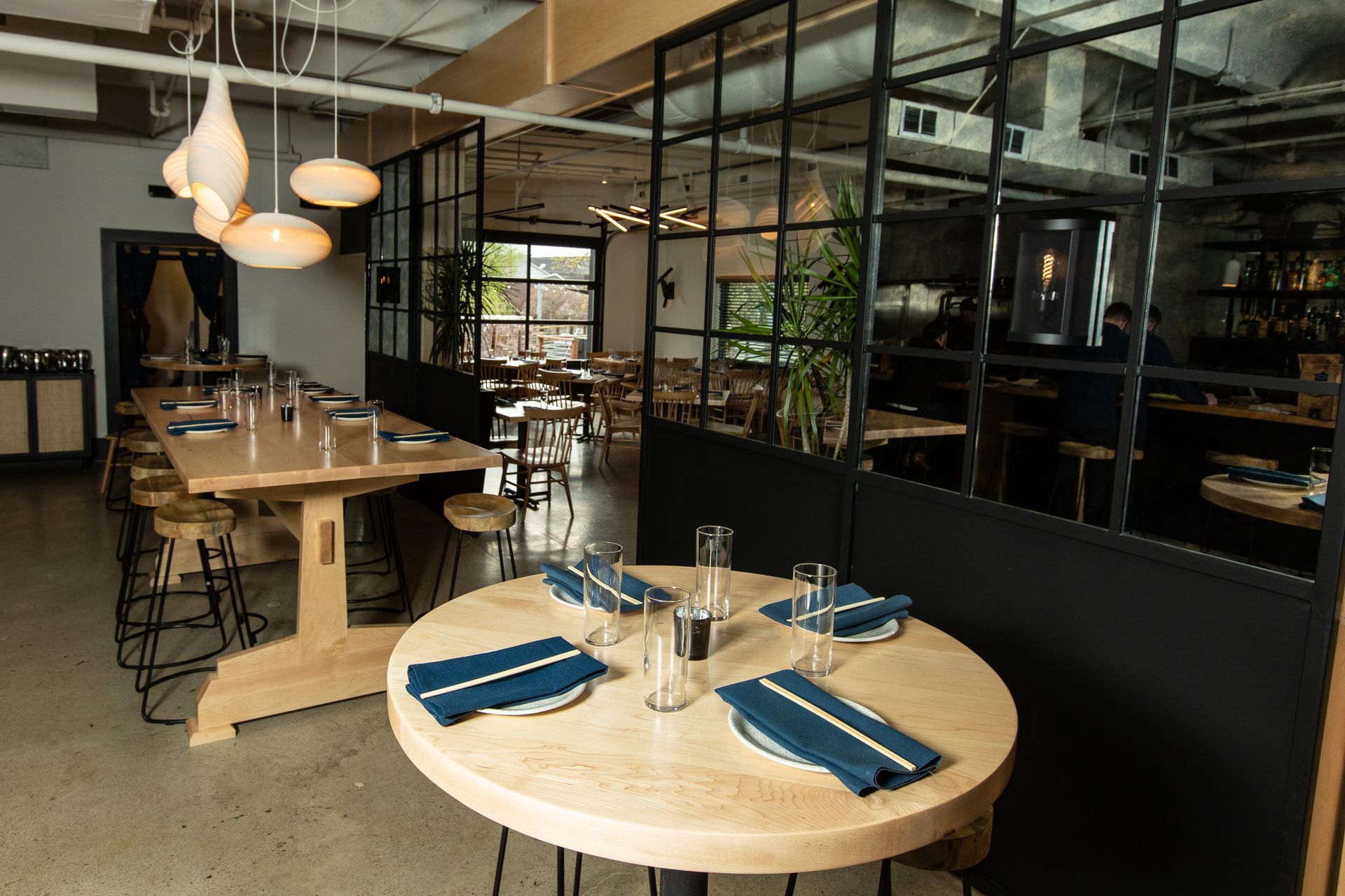 Modern restaurant interior with wooden tables set with blue napkins and pendant lights hanging overhead