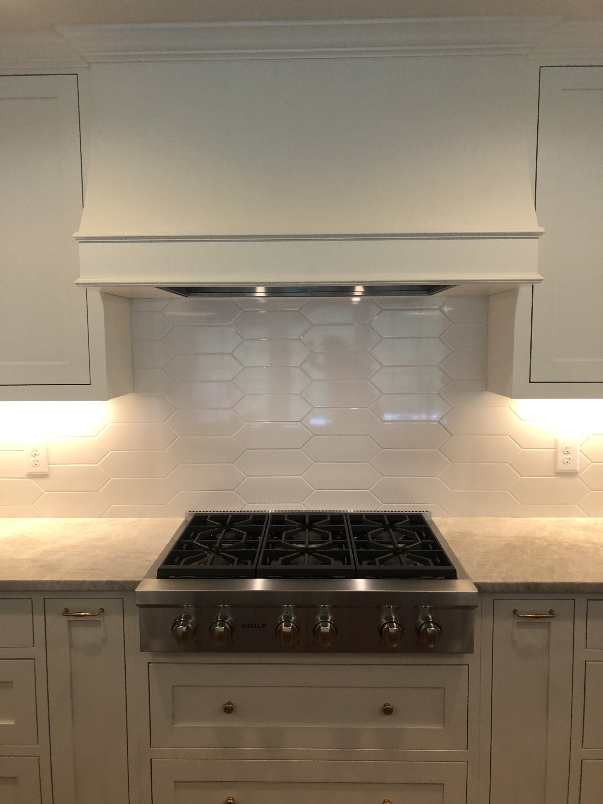Modern kitchen with white cabinets, tiled backsplash, stainless stove, and illuminated under-cabinet lights.