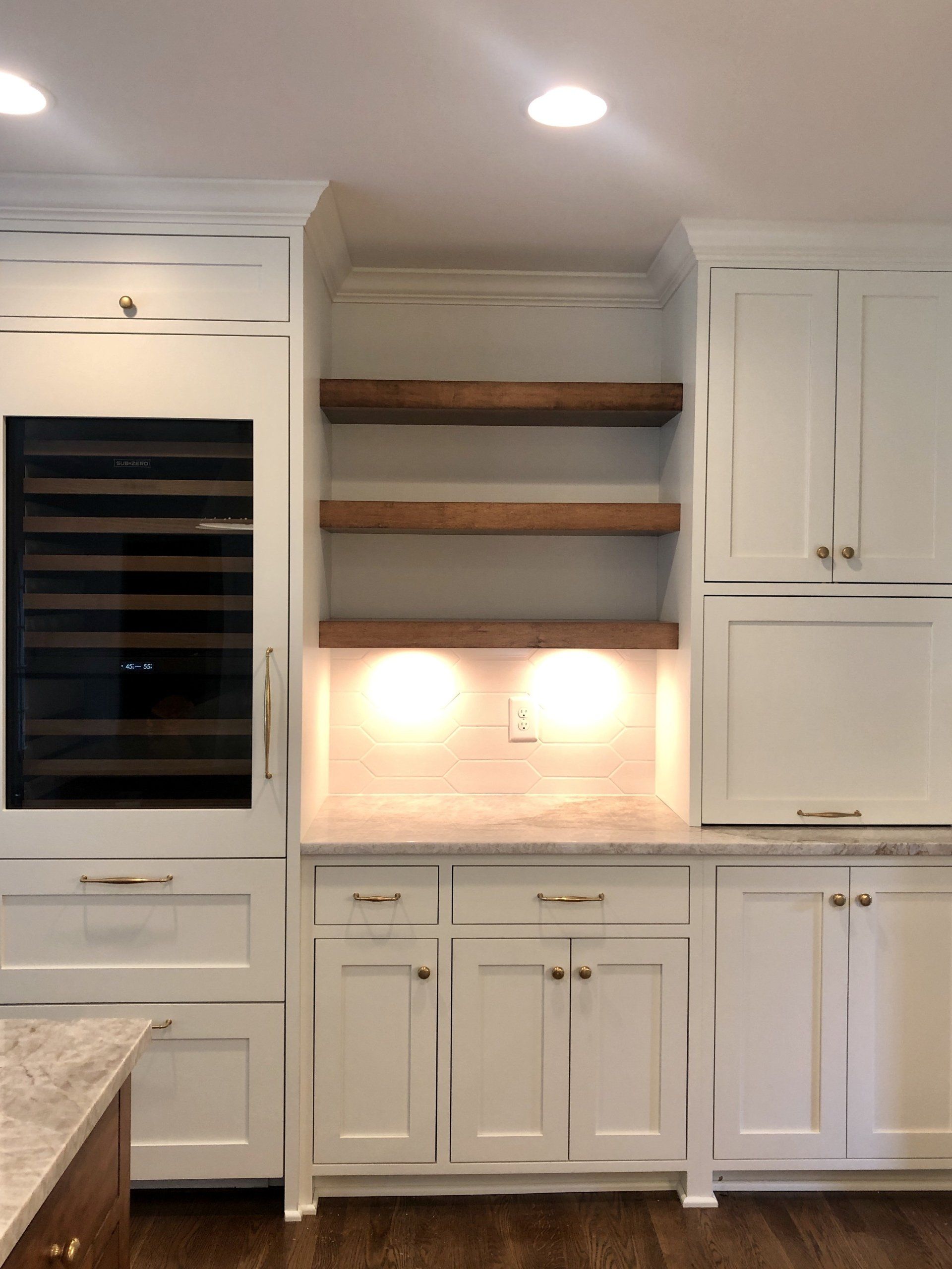 White kitchen with built-in wine cooler, open shelves, and under-cabinet lighting above a countertop.