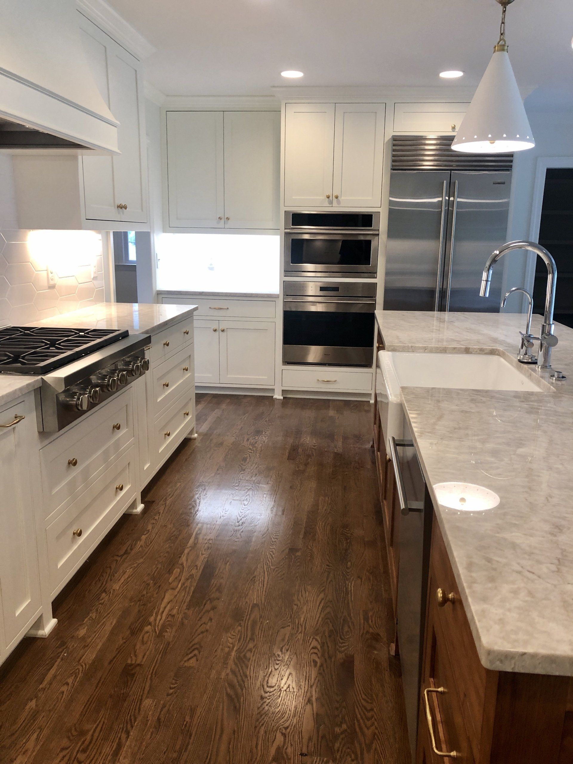 Bright white kitchen with stainless appliances, marble island, and dark hardwood floor