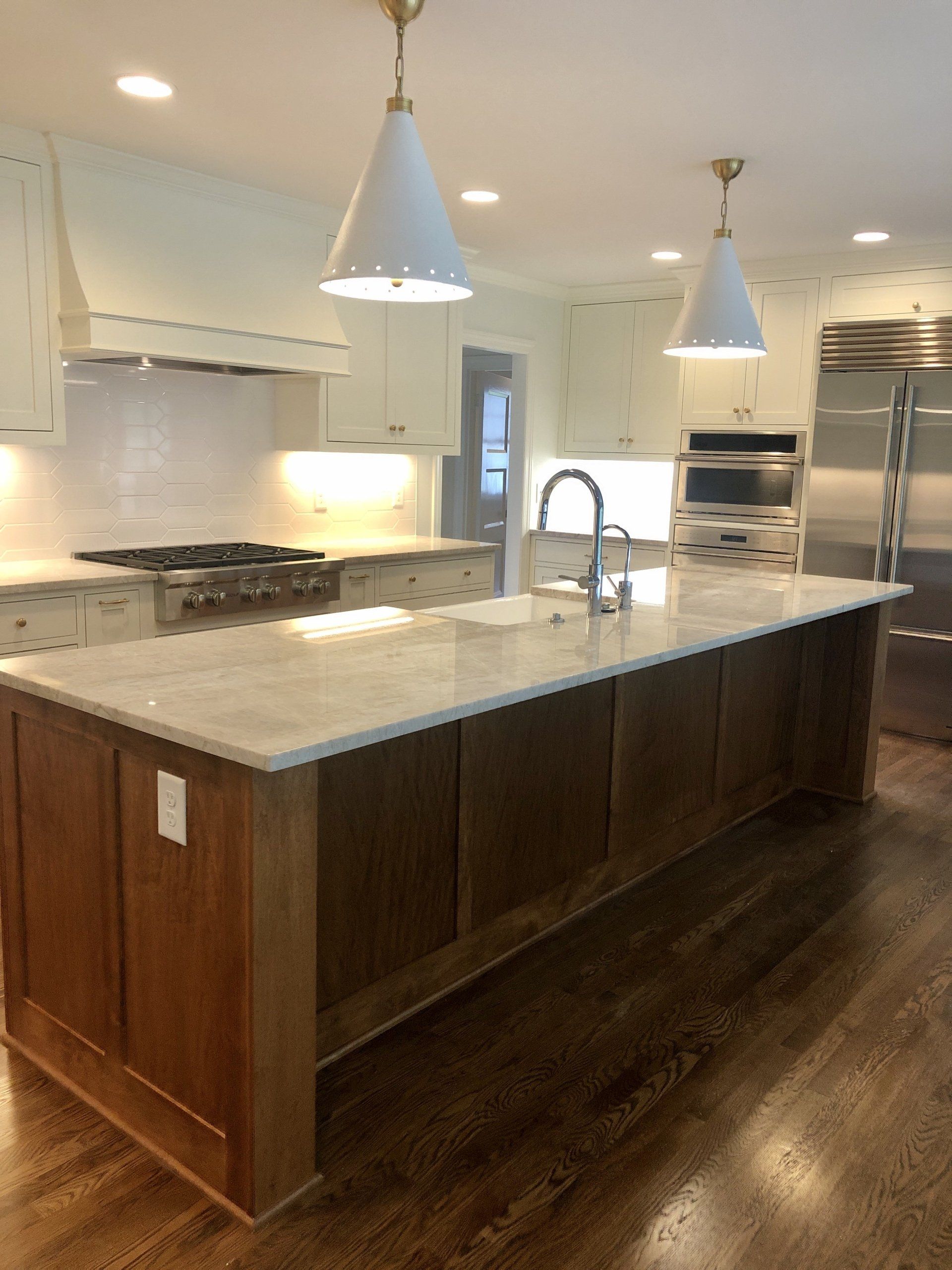 Modern kitchen with large marble island, wood cabinets, stainless steel appliances, and pendant lights.