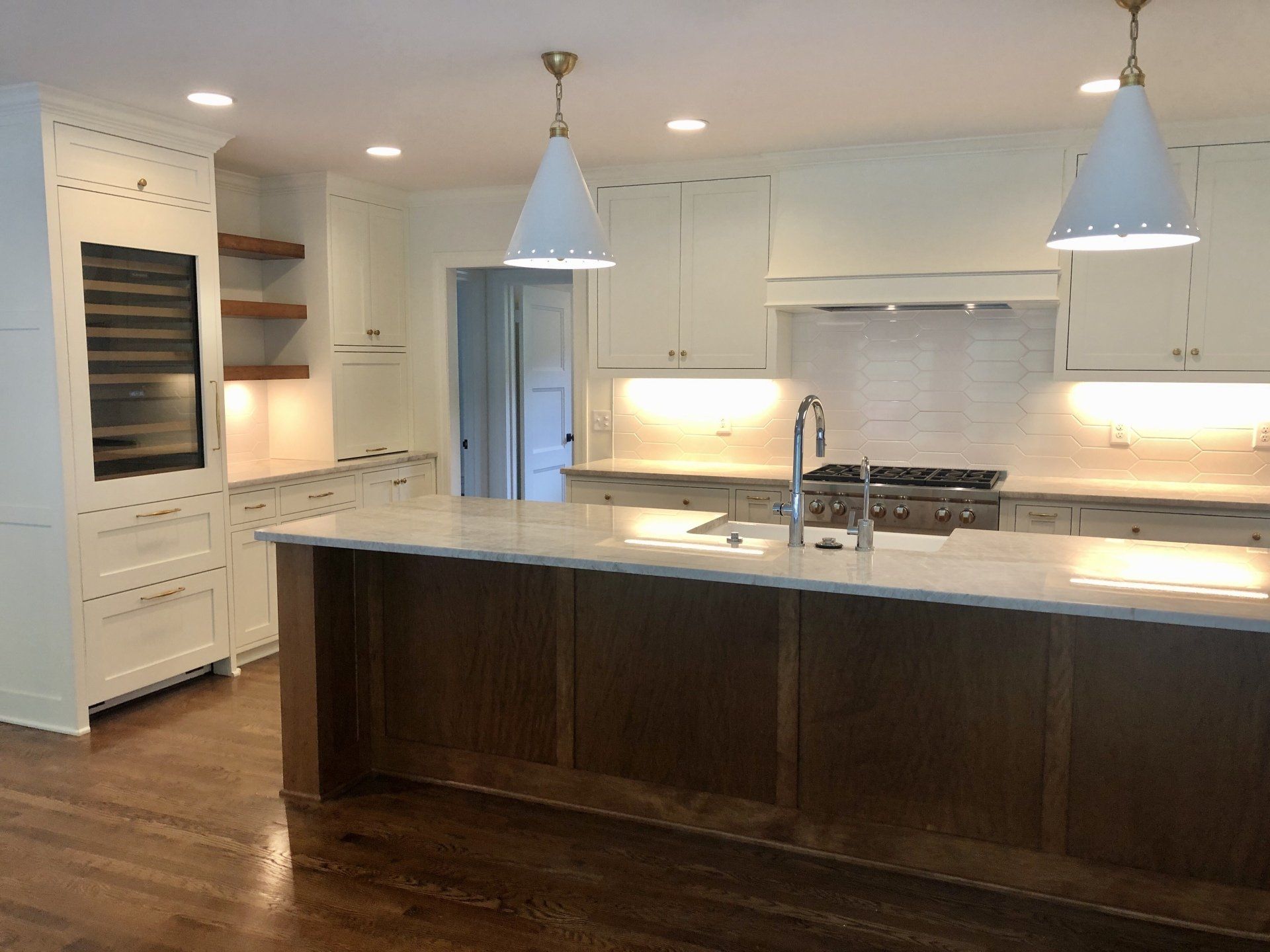 Modern white kitchen with dark wood island, stainless appliances, and pendant lights