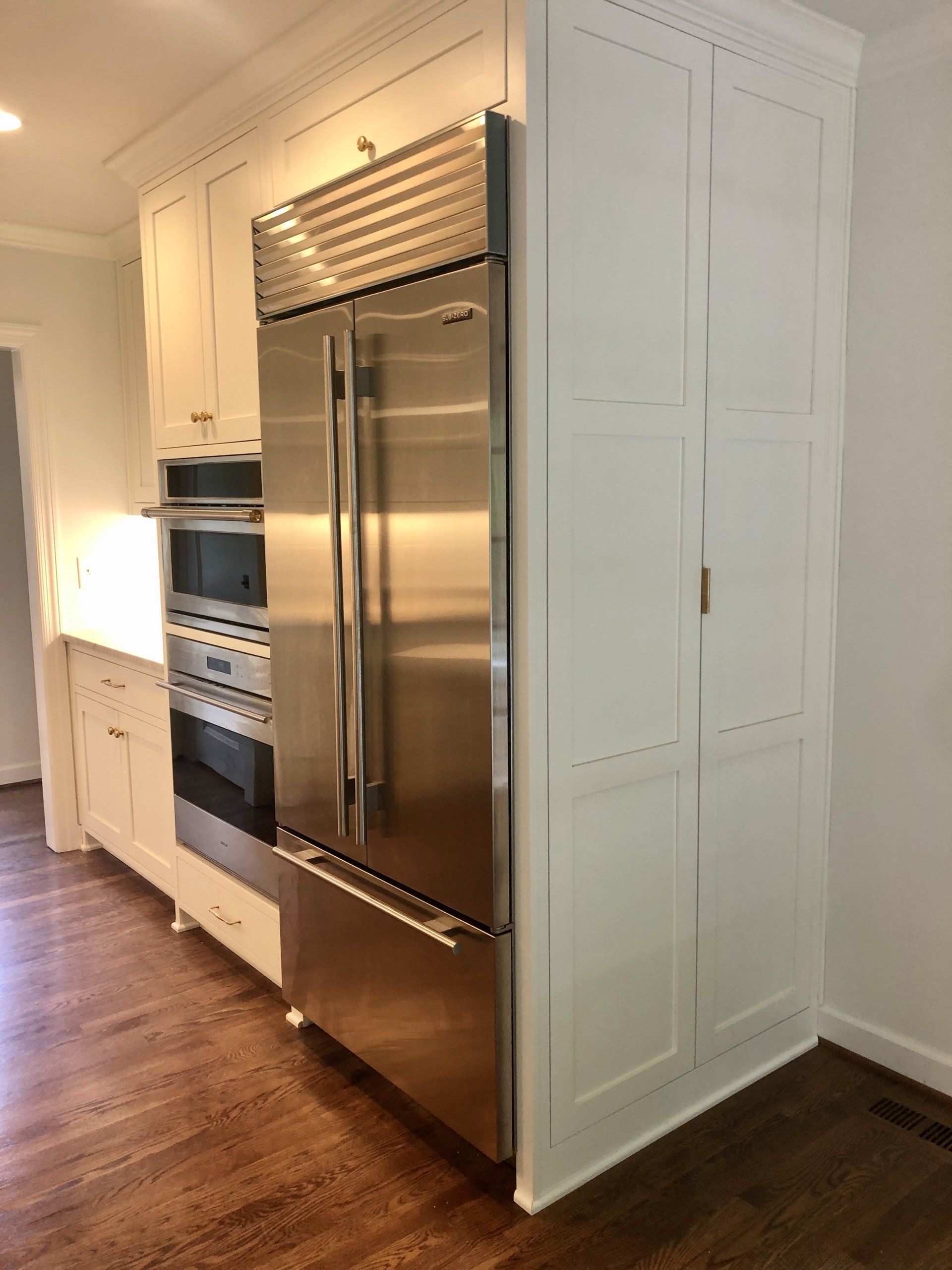 Kitchen with stainless steel double refrigerator and built-in ovens in white cabinetry