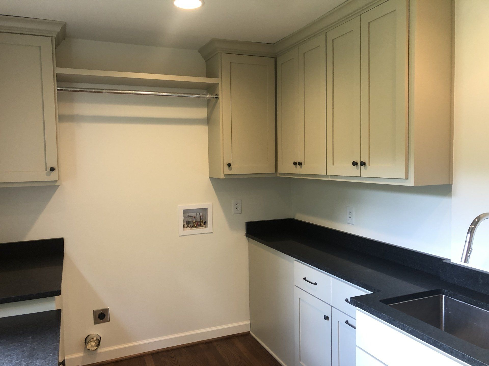 Empty kitchen with cream cabinets, black countertops, sink, and a bare wall opening for appliances