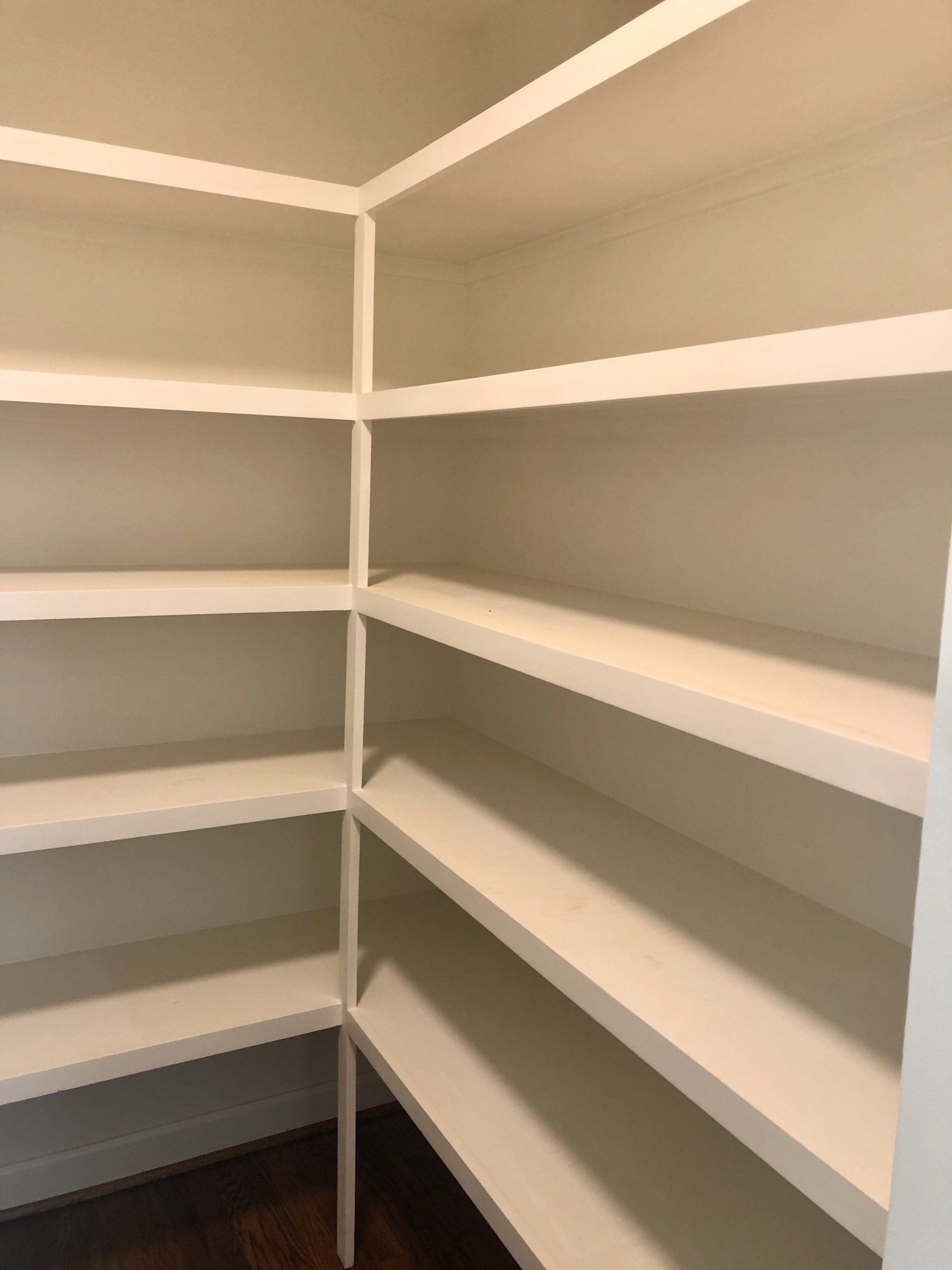 Empty corner pantry with white shelves and gray walls