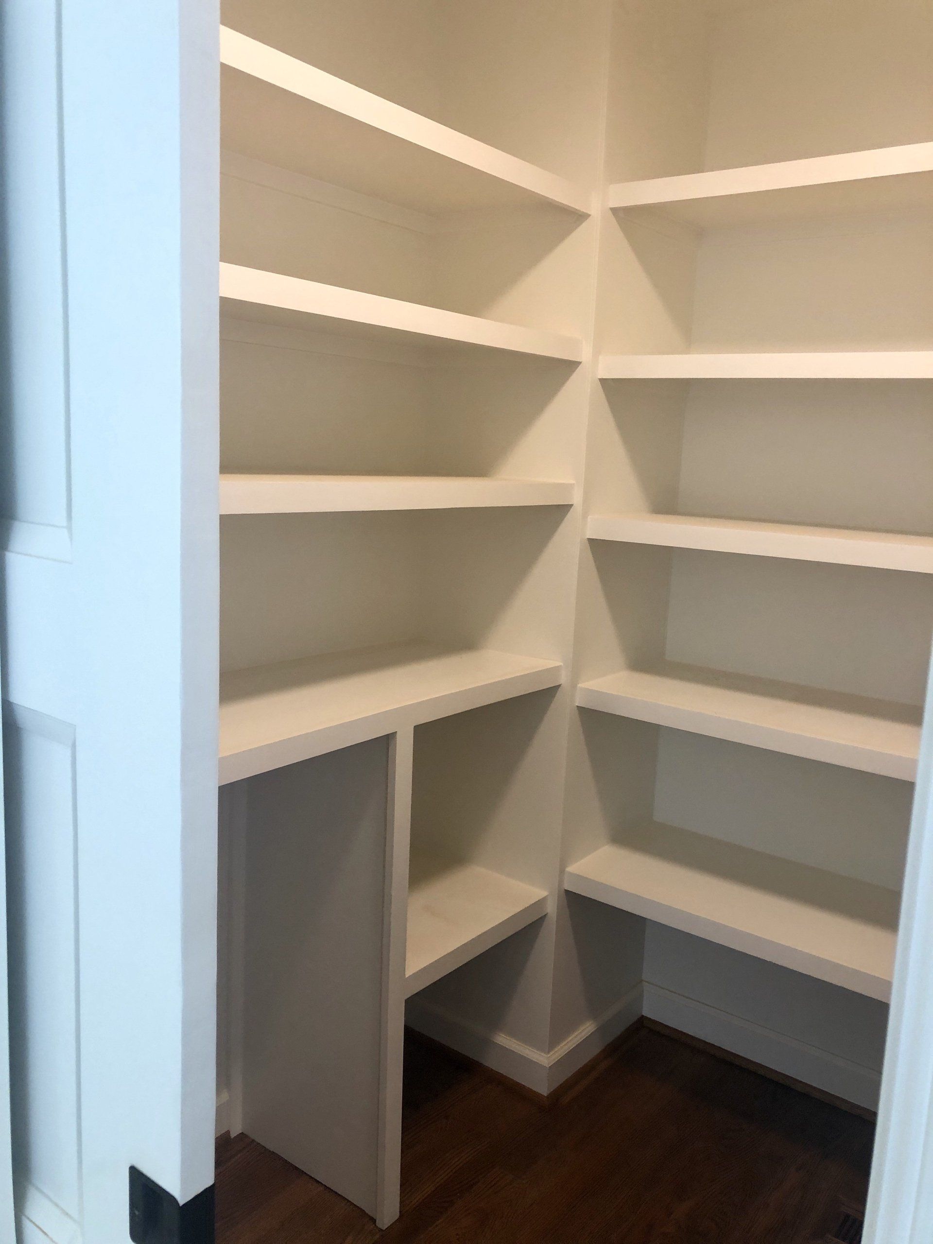 Empty white corner shelving with multiple shelves and a small lower cabinet in a closet or pantry.