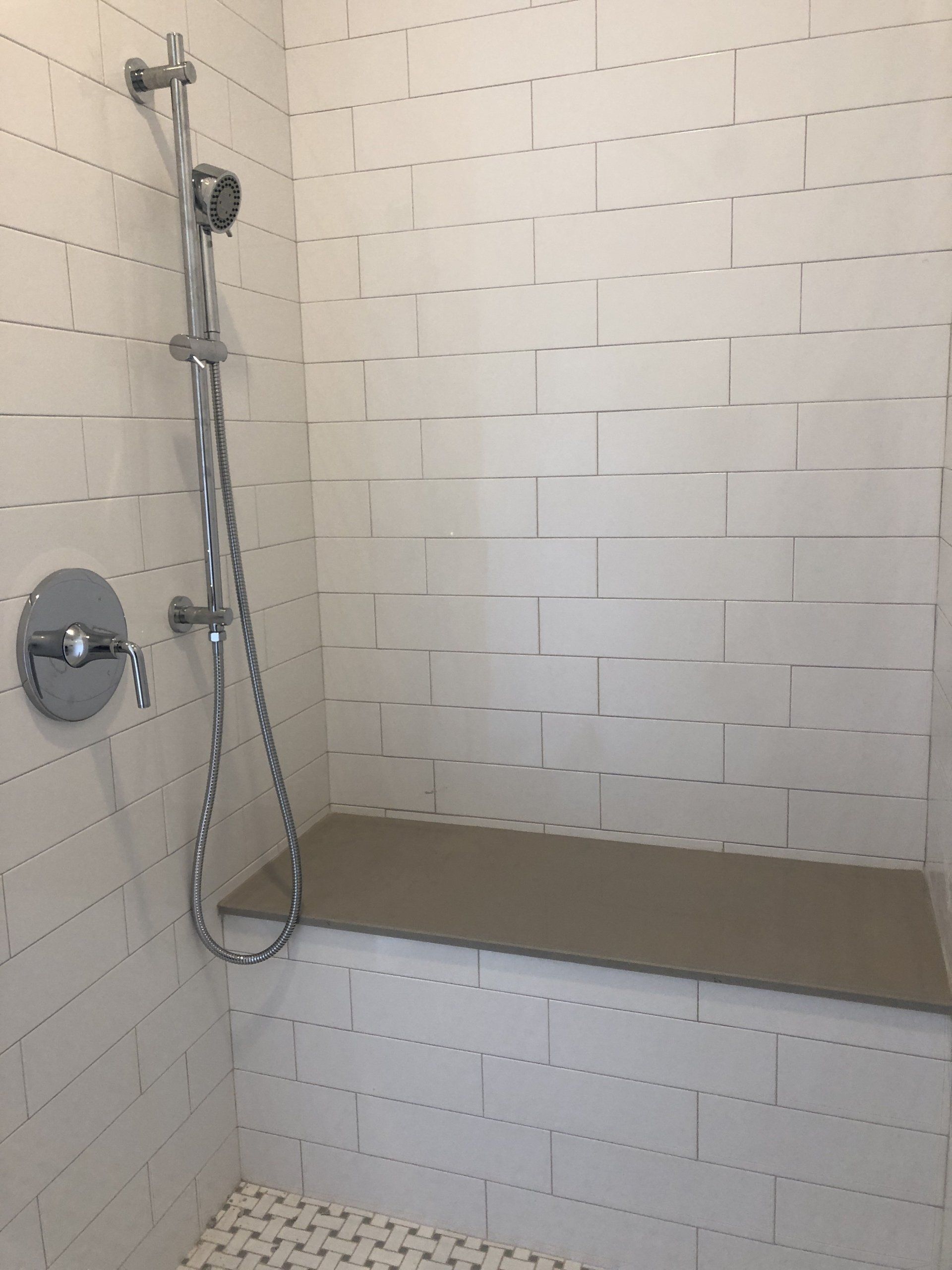 Accessible shower with white tile walls, handheld showerhead, and built-in bench seat