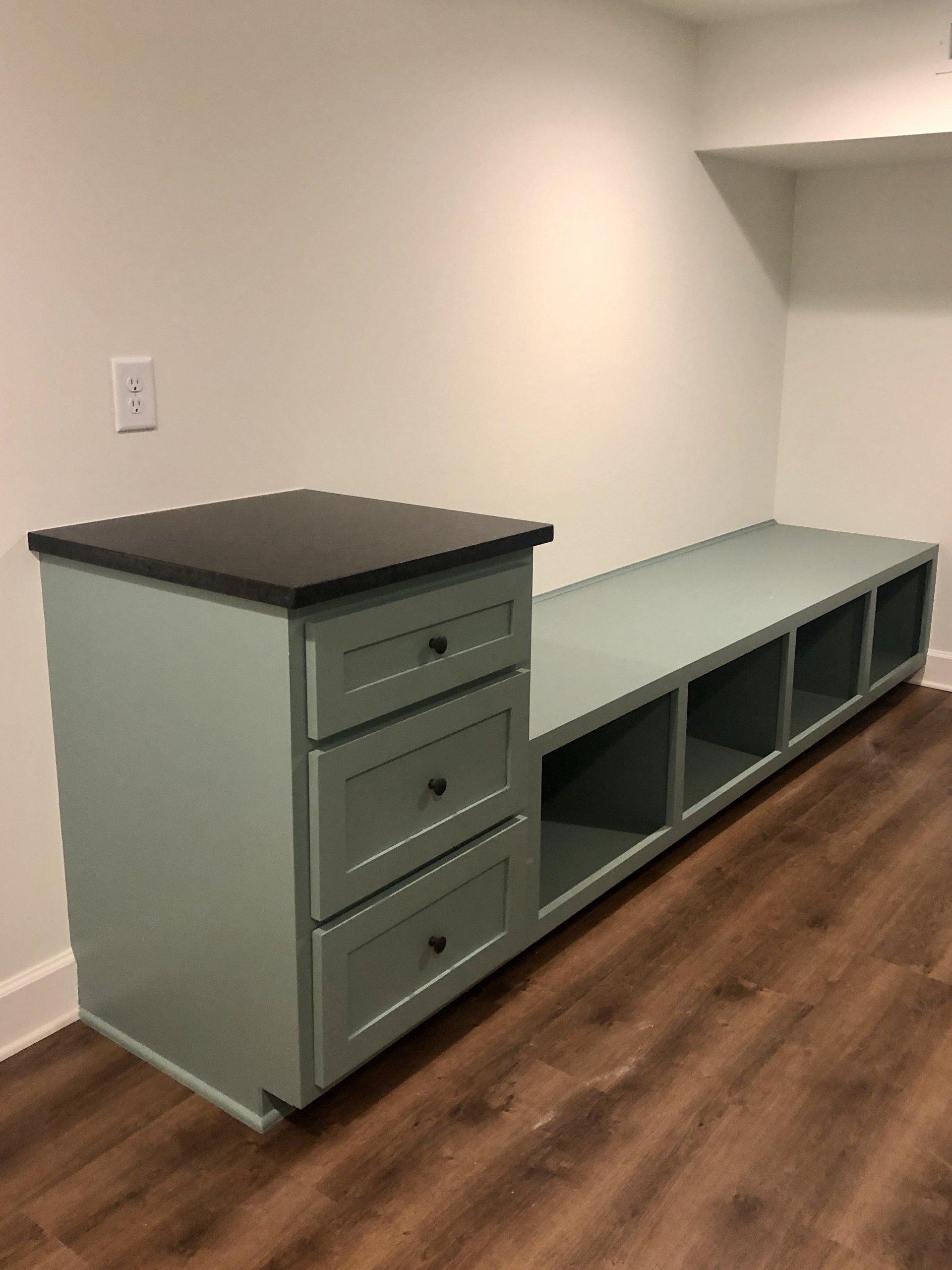 Green built-in bench with drawers and cubbies against a wall in a room with wood flooring
