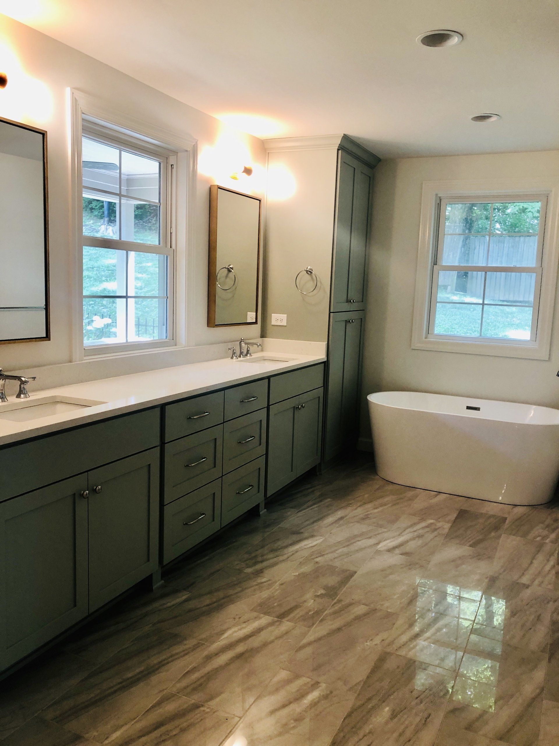 Modern bathroom with double vanity, mirror, windows, and a freestanding tub on wood-look tile floor