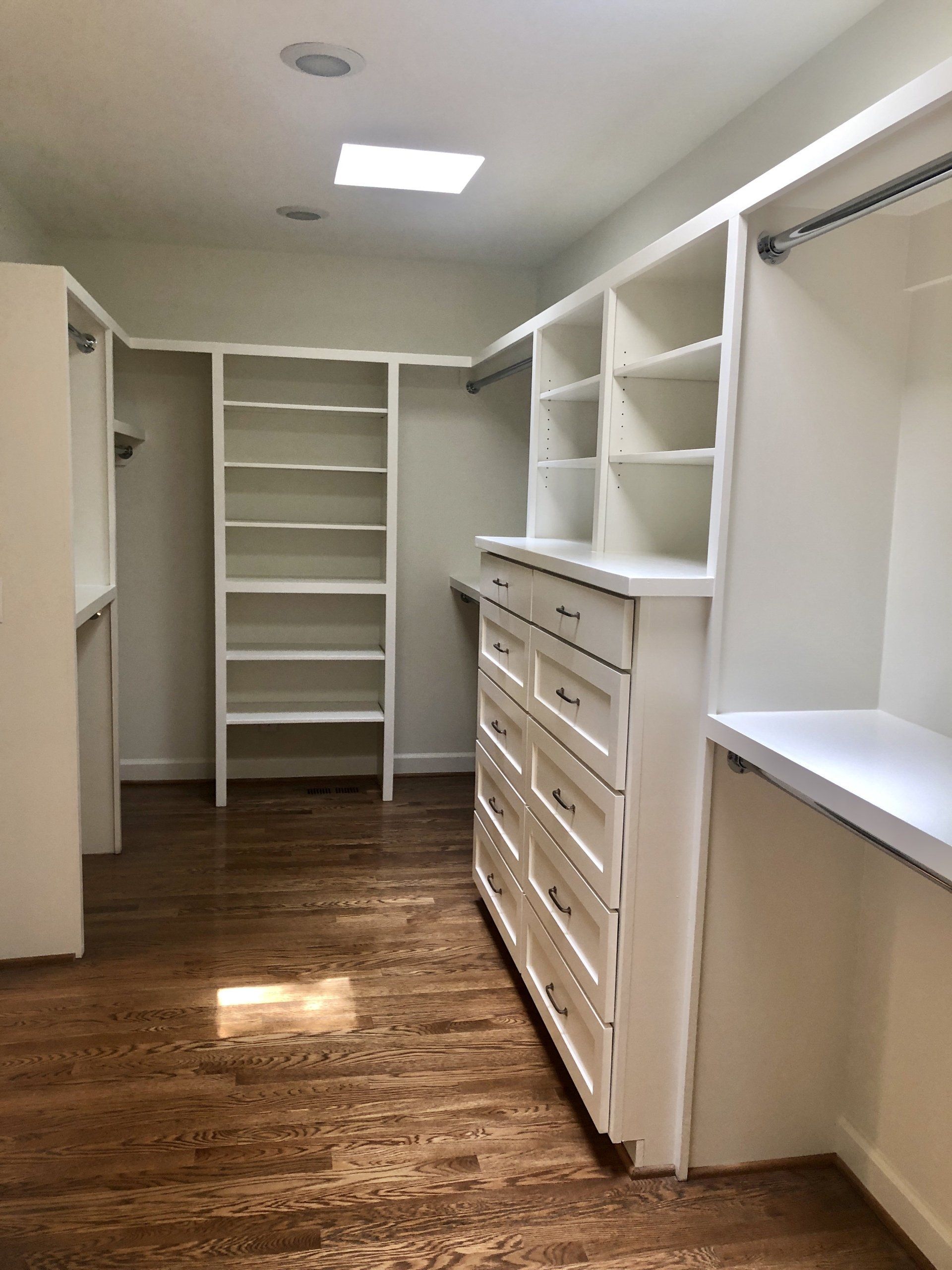Walk-in closet with white shelves and drawers, open hanging rod, and wood flooring