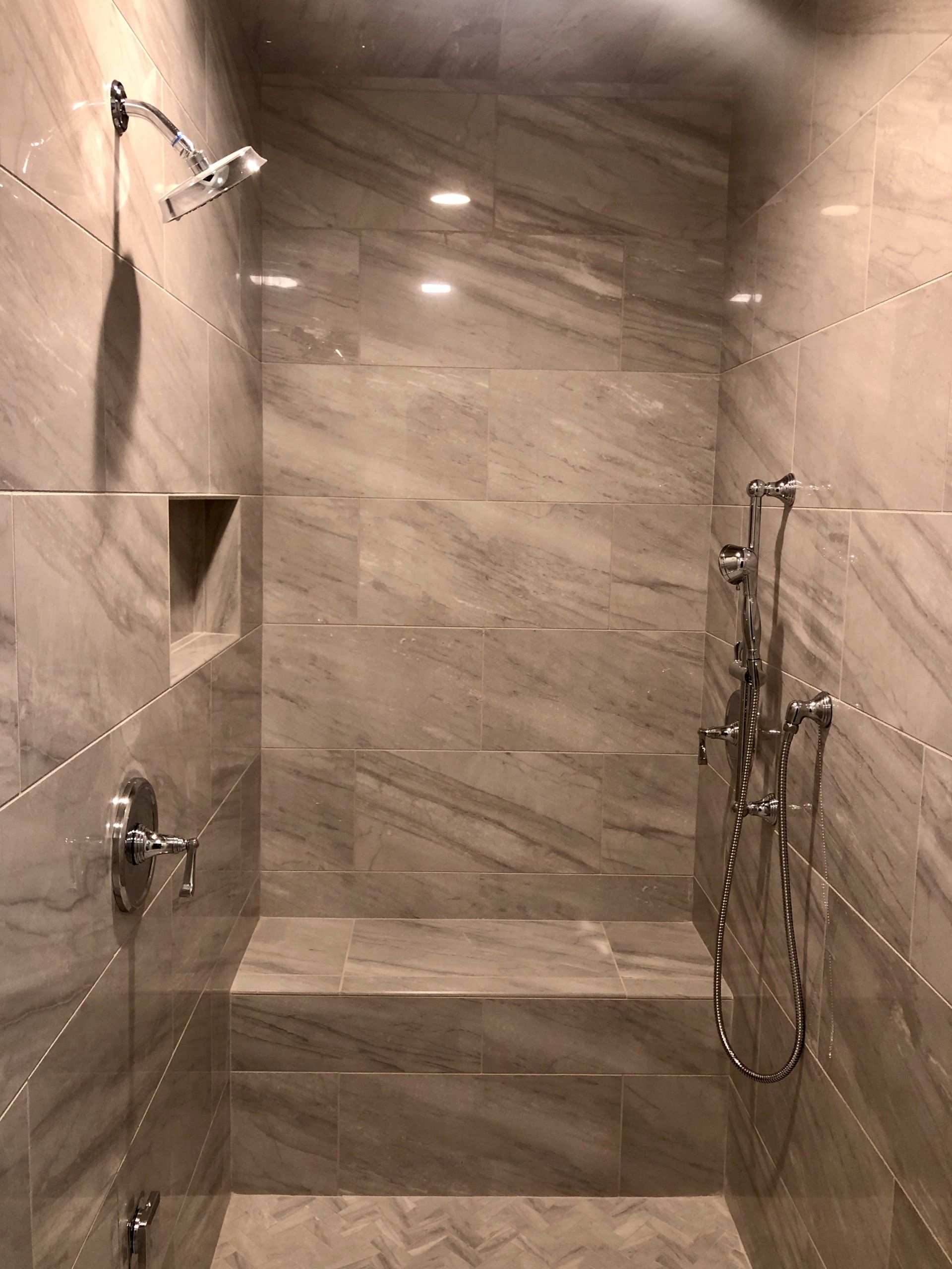 Modern marble-tiled walk-in shower with glass enclosure, wall showerhead, and built-in shelf.