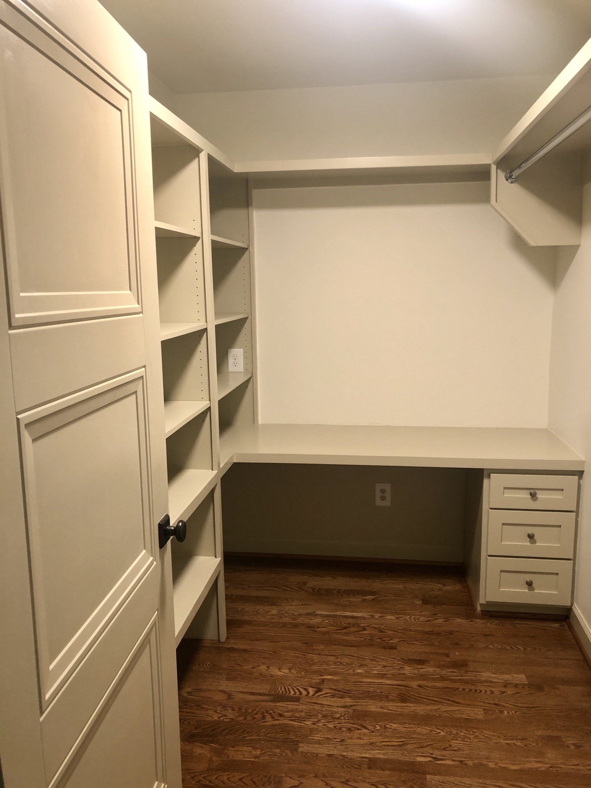 Empty walk-in closet with built-in shelves, hanging rods, desk nook, and wood floor.