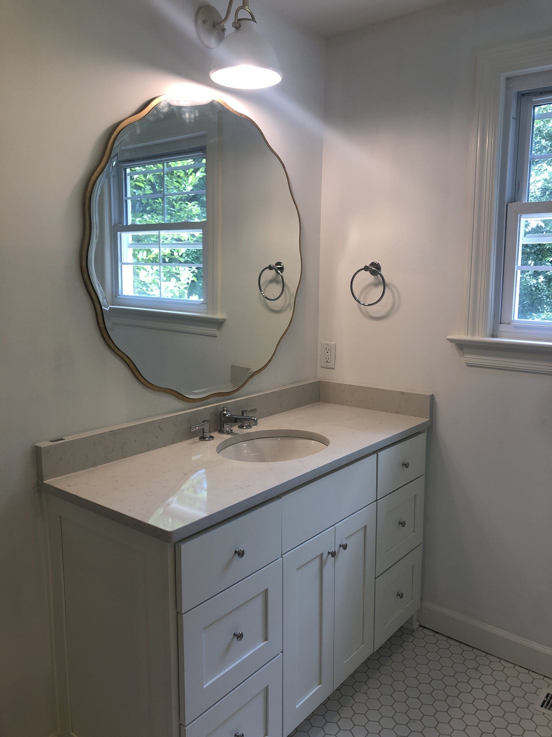 Bathroom vanity with octagonal mirror, white sink, and window