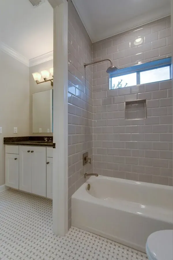 Bathroom with tiled shower-tub combo, white vanity, and small window above the tub.