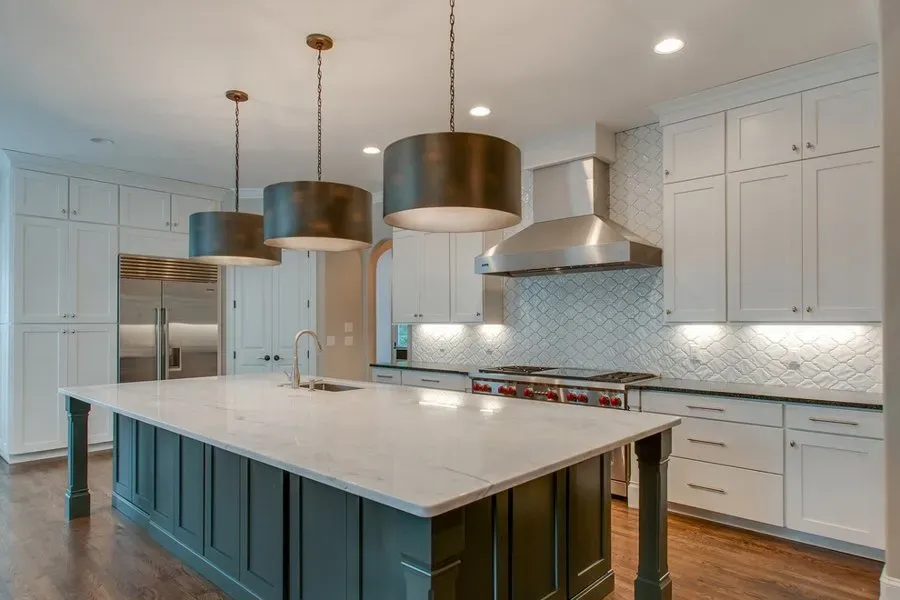 Modern white kitchen with large island, pendant lights, marble countertop, and stainless steel appliances