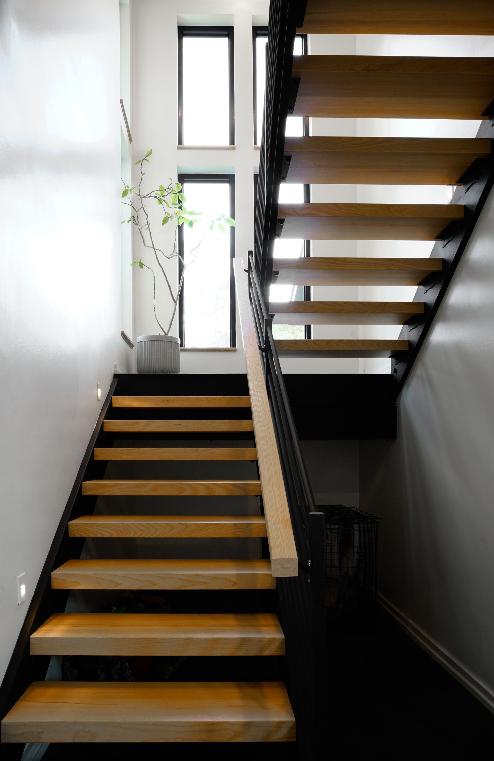 Modern indoor staircase with wooden steps, white walls, and a tall window landing.