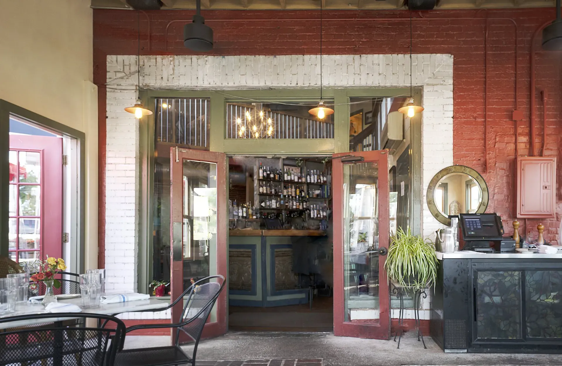 Bright café interior with open double doors, red brick wall, and tables by the window.