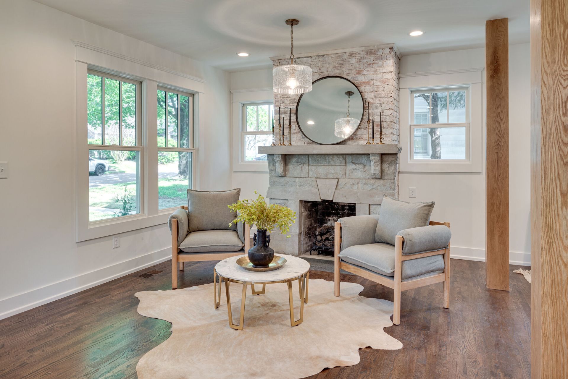 Bright living room with fireplace, gray chairs, round mirror, and cream rug on hardwood floor.