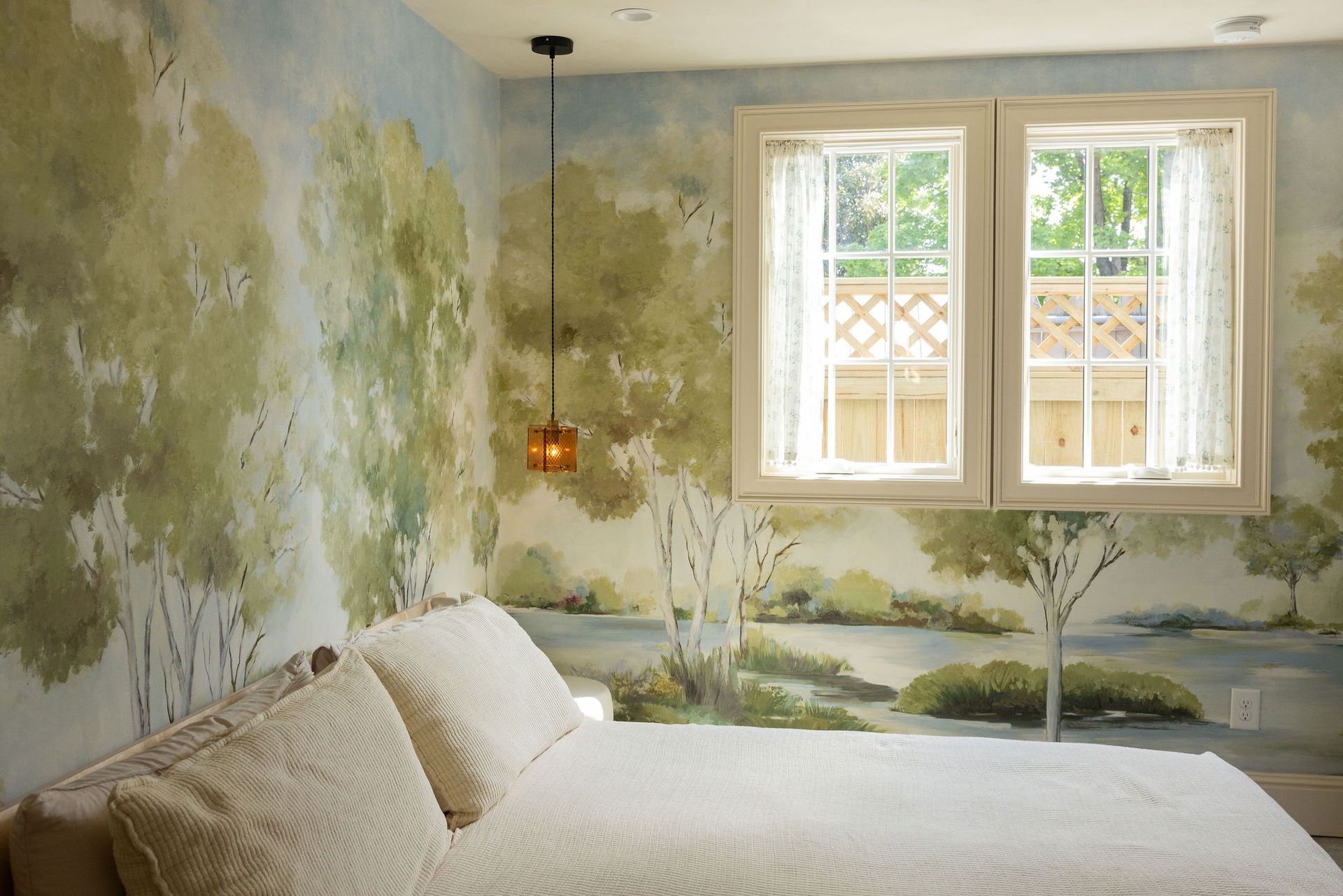 Bedroom with botanical mural walls, white bedding, and a window letting in soft daylight