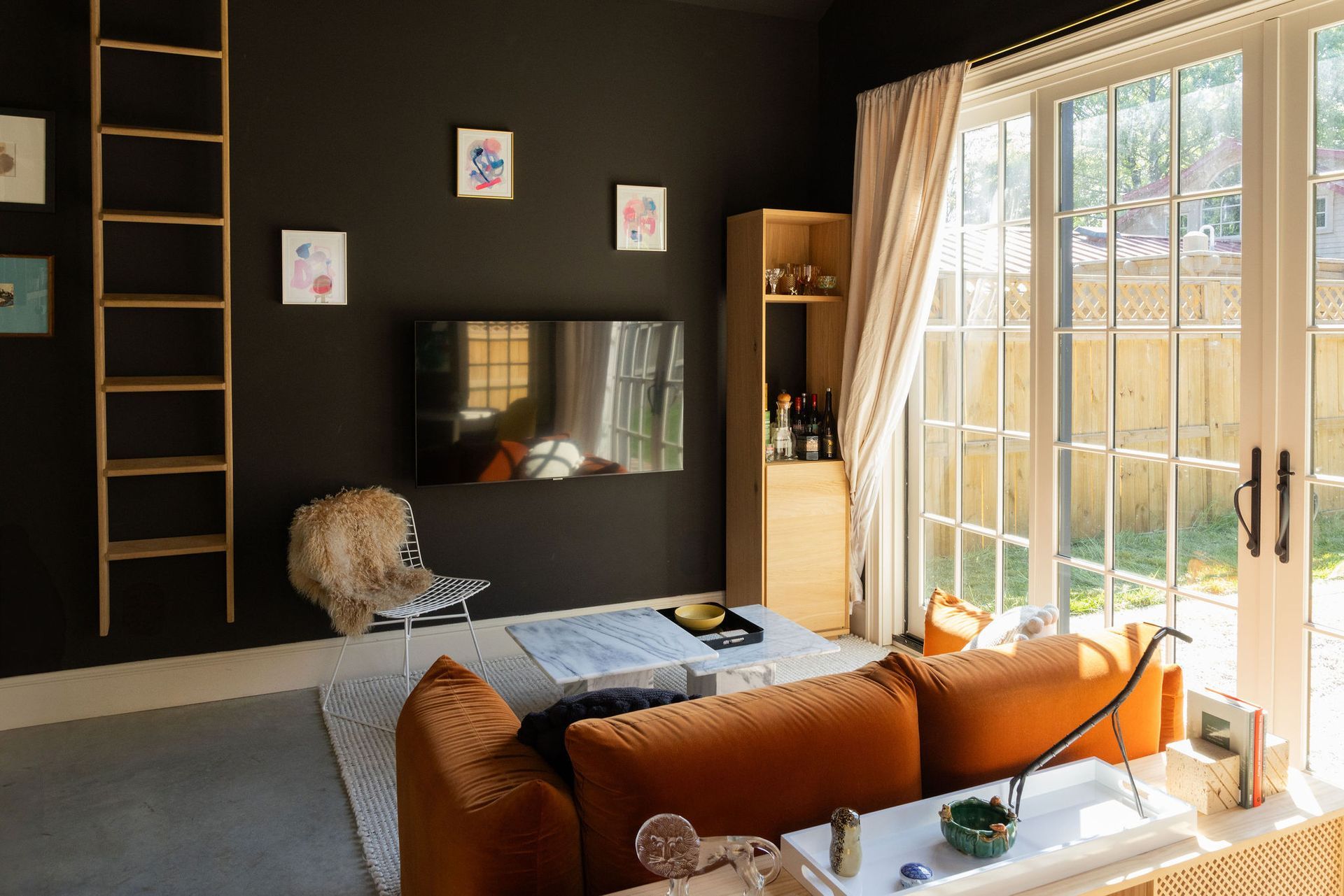 Modern living room with black accent wall, orange sofa, TV, and floor-to-ceiling windows
