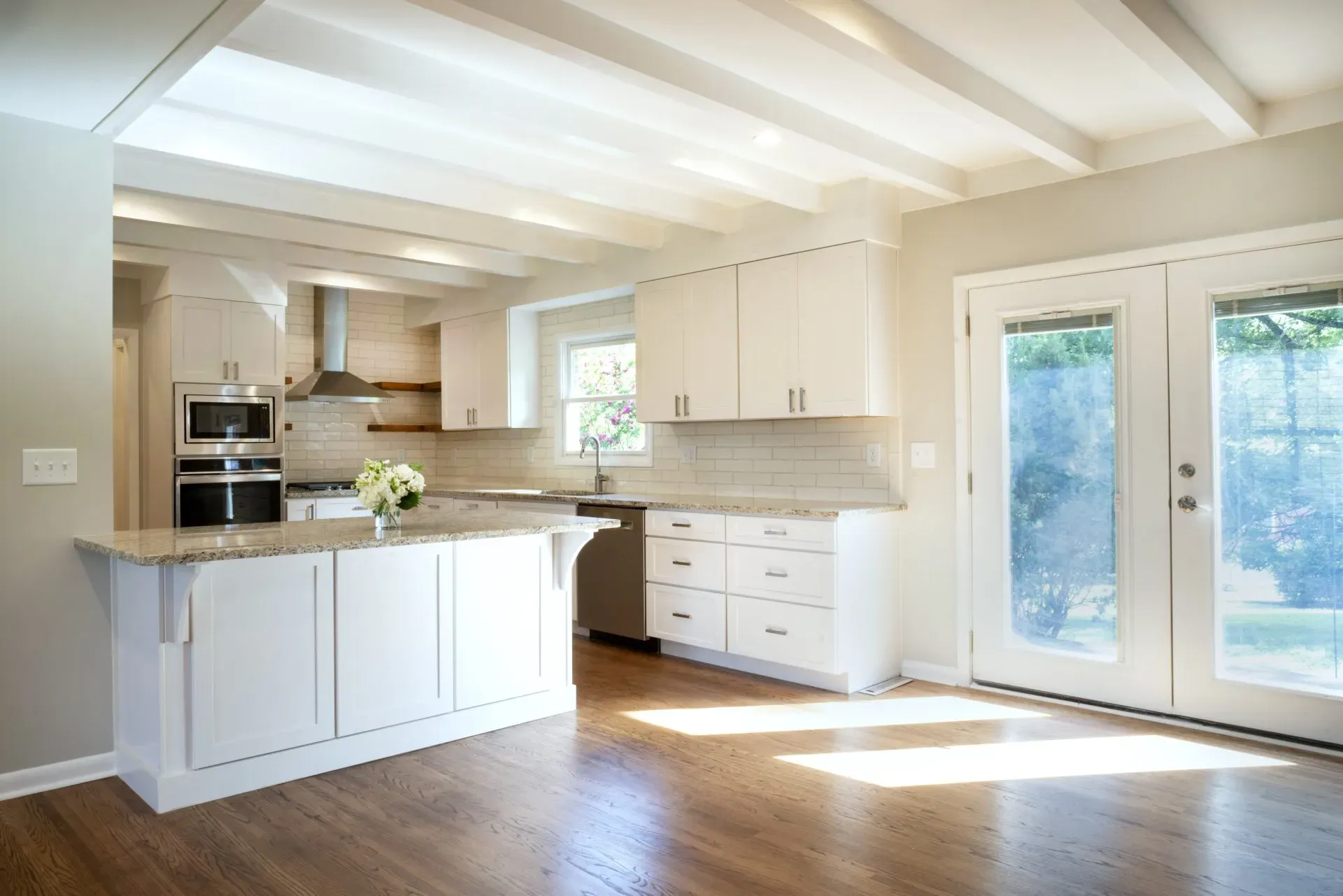 Bright modern kitchen with white cabinets, island, wood floors, and glass doors to a sunlit patio