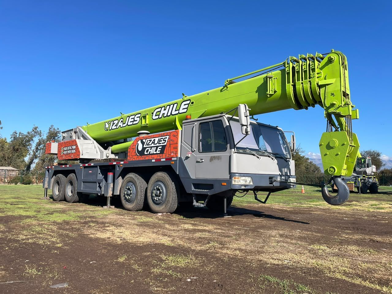 Grúa móvil verde brillante aparcada sobre un terreno irregular bajo un cielo azul