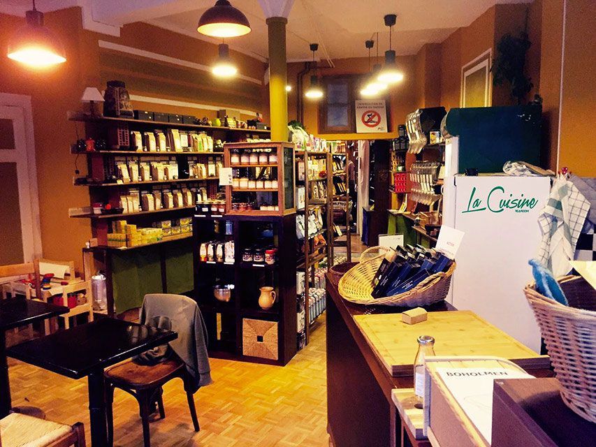 Intérieur d'une petite boutique avec des étagères de marchandises, un comptoir et des tables. Éclairage doux aux tons naturels.
