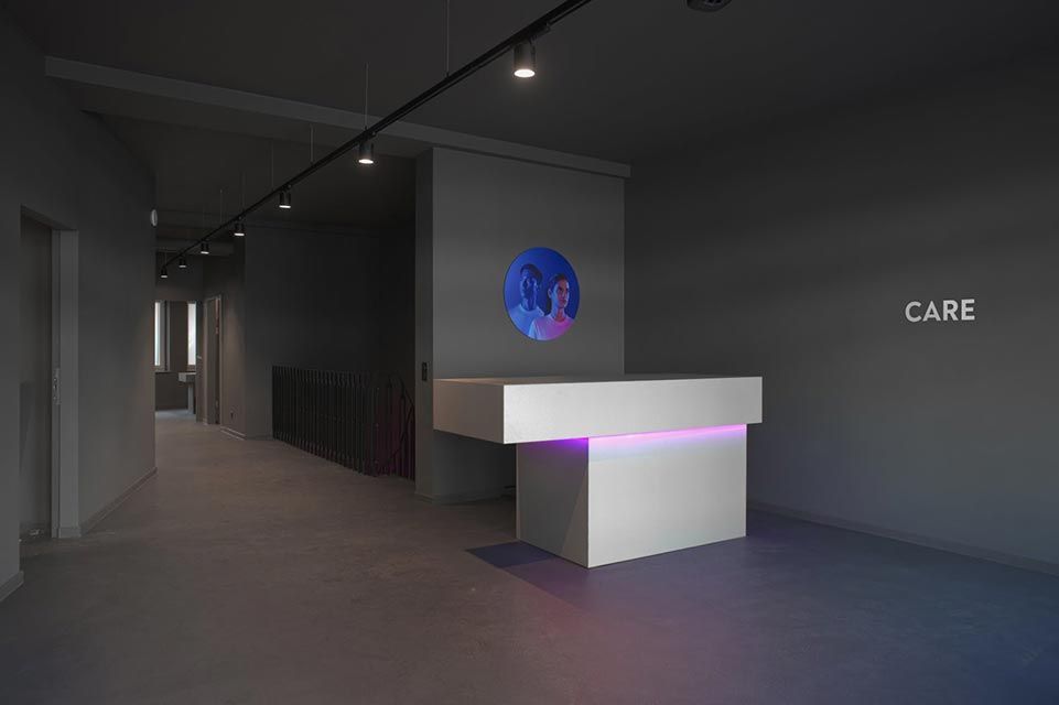 Espace d'accueil moderne avec un bureau blanc, un éclairage violet et un écran circulaire mural. Inscription « CARE » au mur.