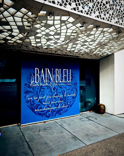 Enseigne bleue pour le spa « Le Bain Bleu », texte blanc sur fond bleu, plafond à motifs, extérieur en béton.