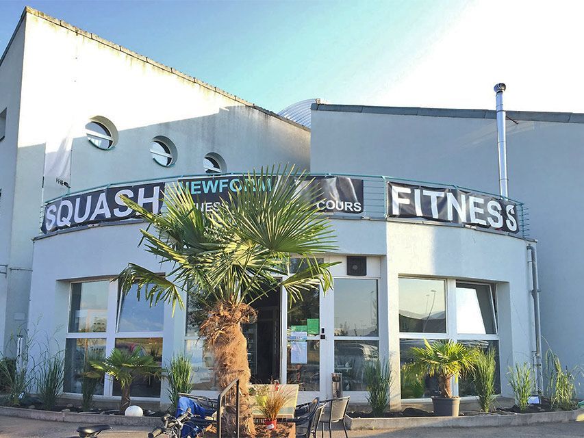 Bâtiment de Squash Fitness avec un palmier devant. L'enseigne indique « Squash Fitness ».