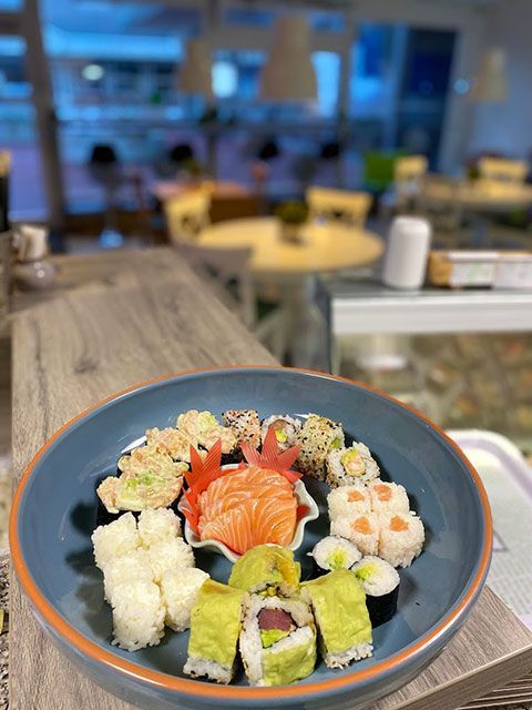 Plateau de sushis avec un assortiment de rouleaux, saumon et avocat sur une assiette bleue, en intérieur.