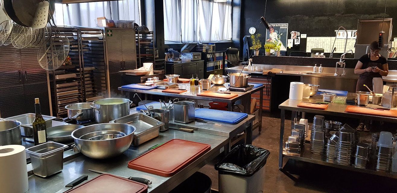 Une cuisine de restaurant avec des plans de travail en acier inoxydable, des casseroles et une personne qui travaille à l'arrière.