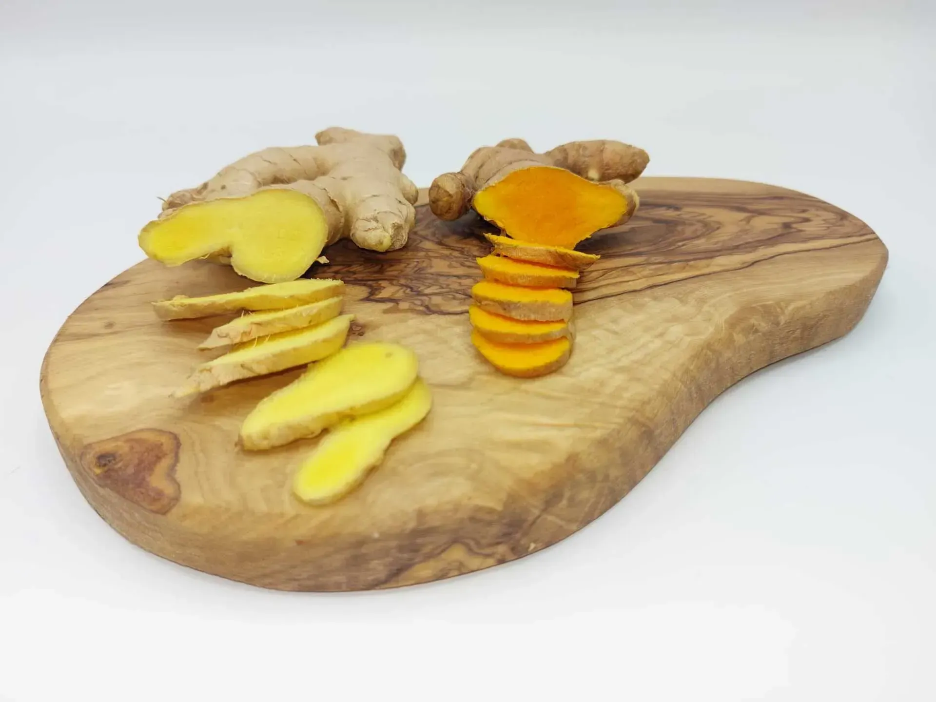 Tranches de gingembre et de curcuma sur une planche à découper en bois, fond blanc.