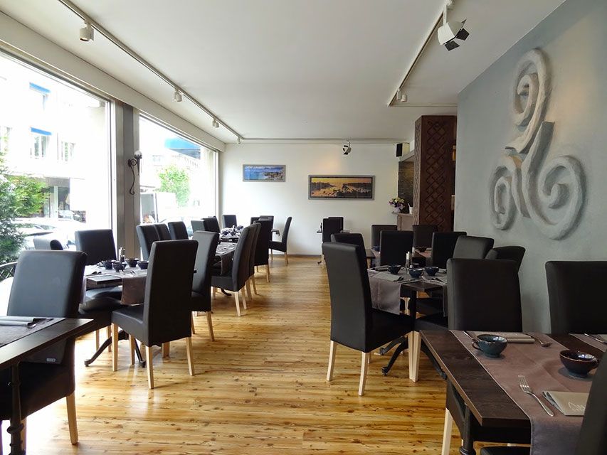 Intérieur de restaurant avec tables et chaises, grandes fenêtres et un élément décoratif mural.