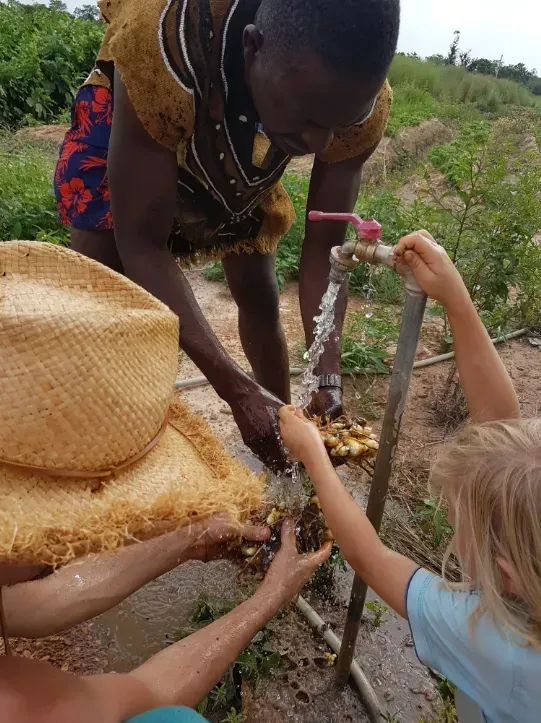 Une personne et des enfants se lavent les mains à l'eau d'un robinet extérieur.