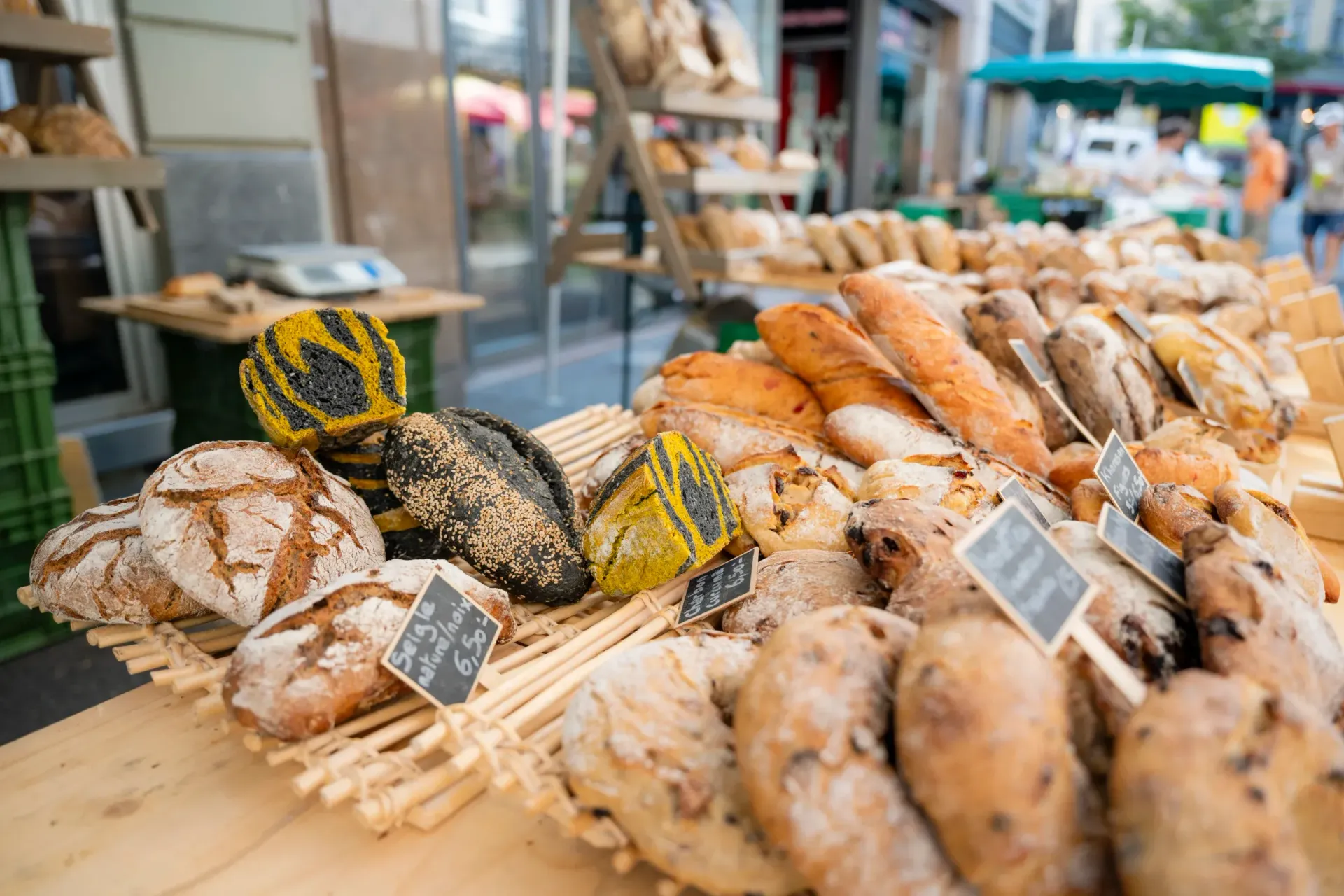 Des pains fraîchement cuits sont exposés sur un marché, notamment des baguettes, des miches et des petits pains.