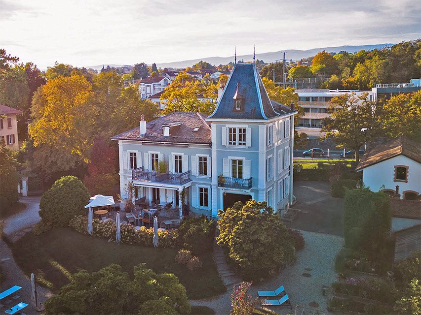 Maison à plusieurs étages bleu clair avec tour, entourée d'arbres, dans un quartier résidentiel.