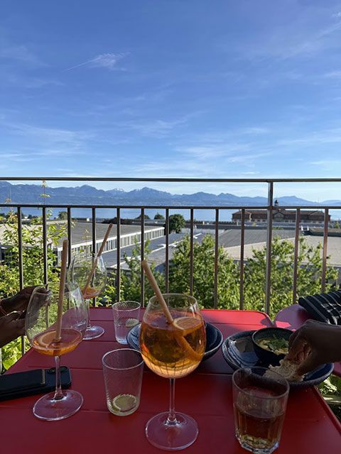 Des cocktails sur une table rouge avec vue sur un lac et des montagnes sous un ciel bleu.