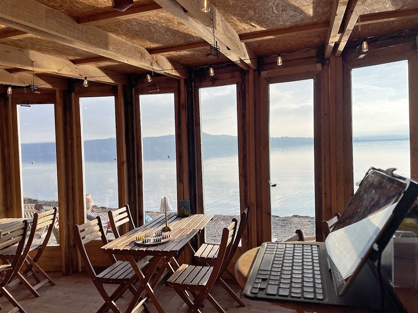 Intérieur d'un café en bois avec vue sur le lac, table dressée et tablette avec clavier utilisée.