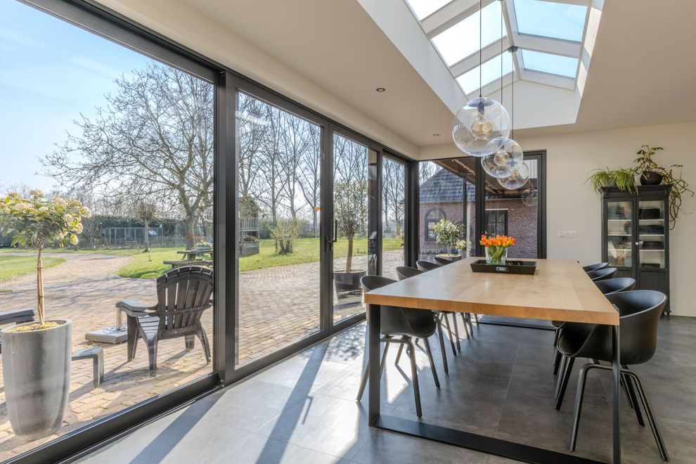 Prachtige moderne eetkamer met een lange houten tafel, zwarte stoelen en grote ramen van vloer tot plafond met uitzicht op een tuin.