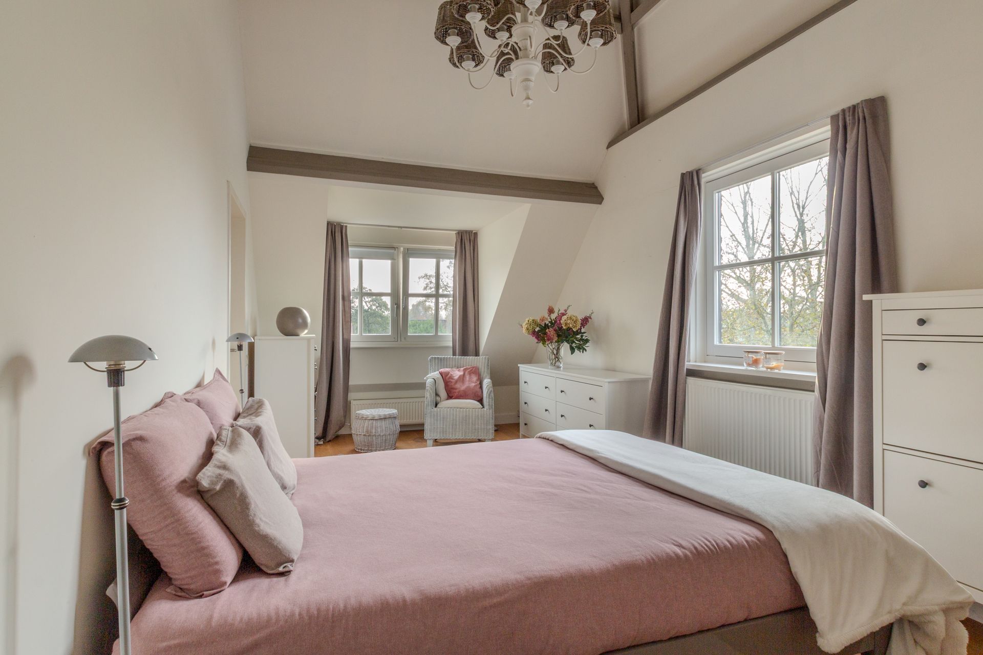 Een lichte, gezellige slaapkamer met een rustige uitstraling (roze en taupe geven de kamer sfeer) en een prachtig hoog plafond, neutrale muren, zichtbare balken.