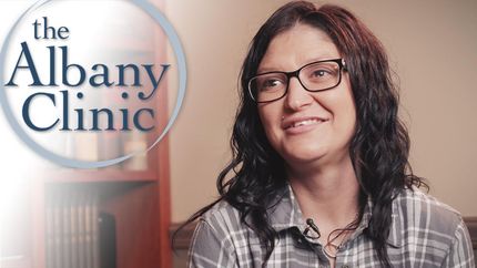 a woman wearing glasses is smiling in front of a sign for the albany clinic