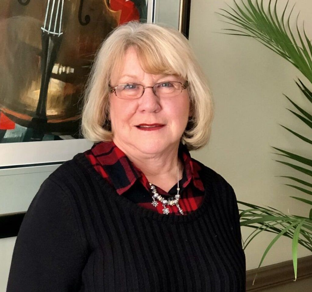 Crystal Knight of the albany clinic wearing glasses and a plaid shirt stands in front of a painting
