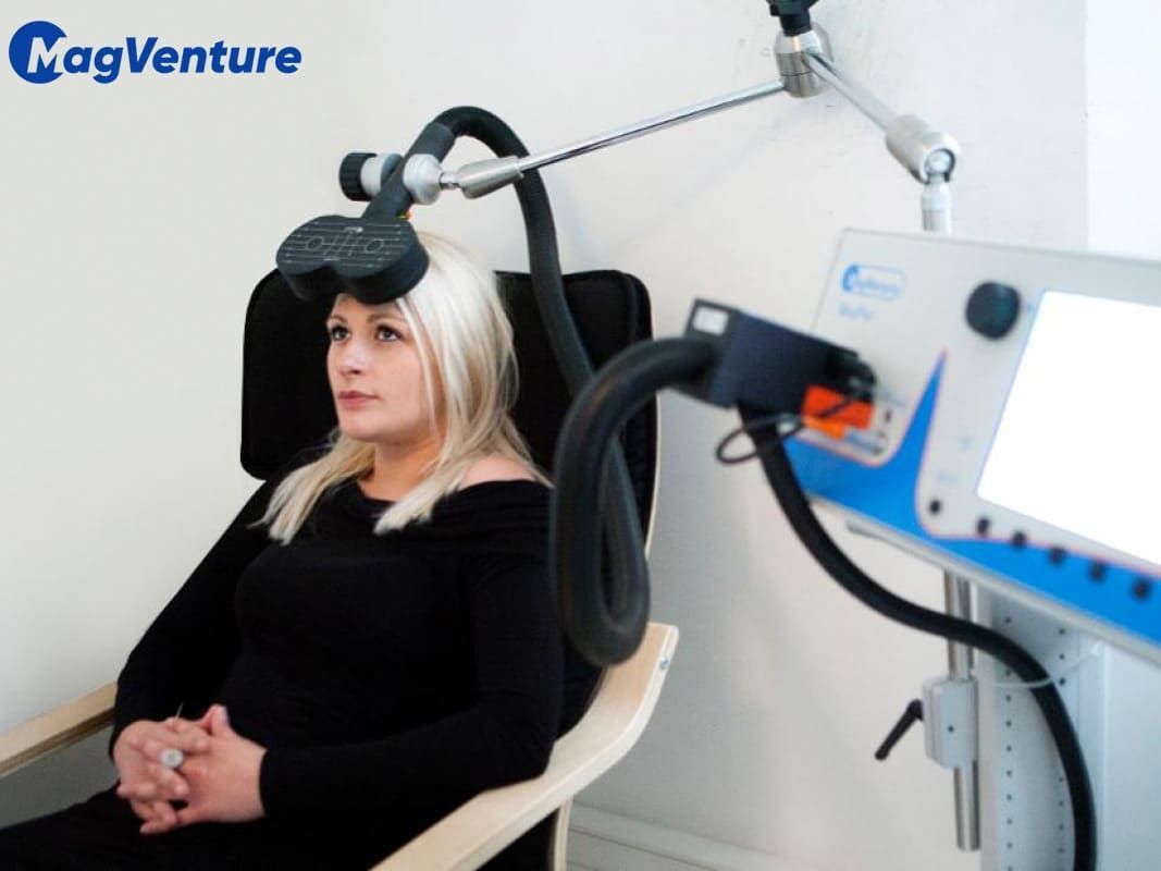 a woman is sitting in front of a Magventure TMS therapy device