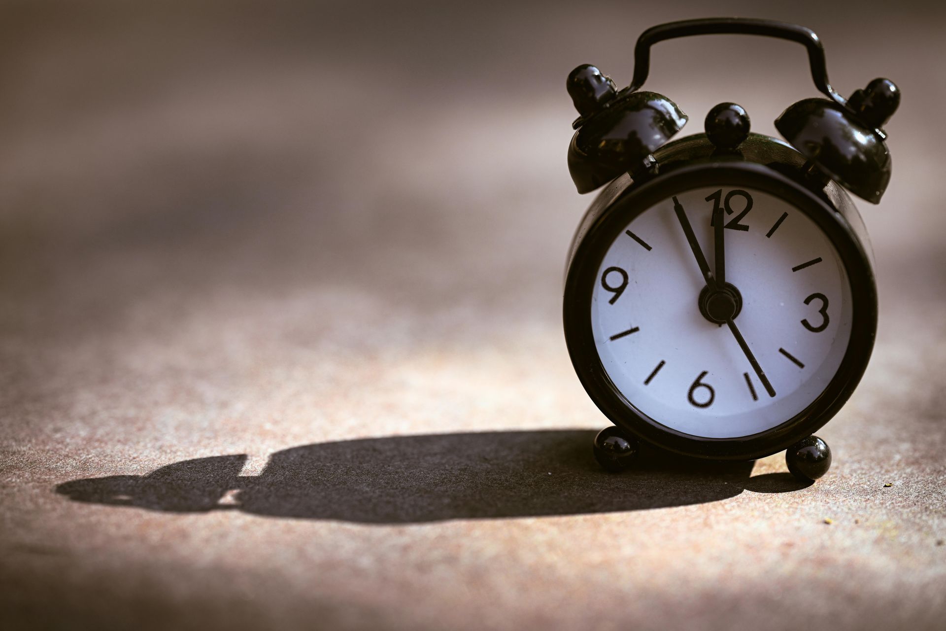 Black alarm clock on a textured surface, casting a long shadow in warm light